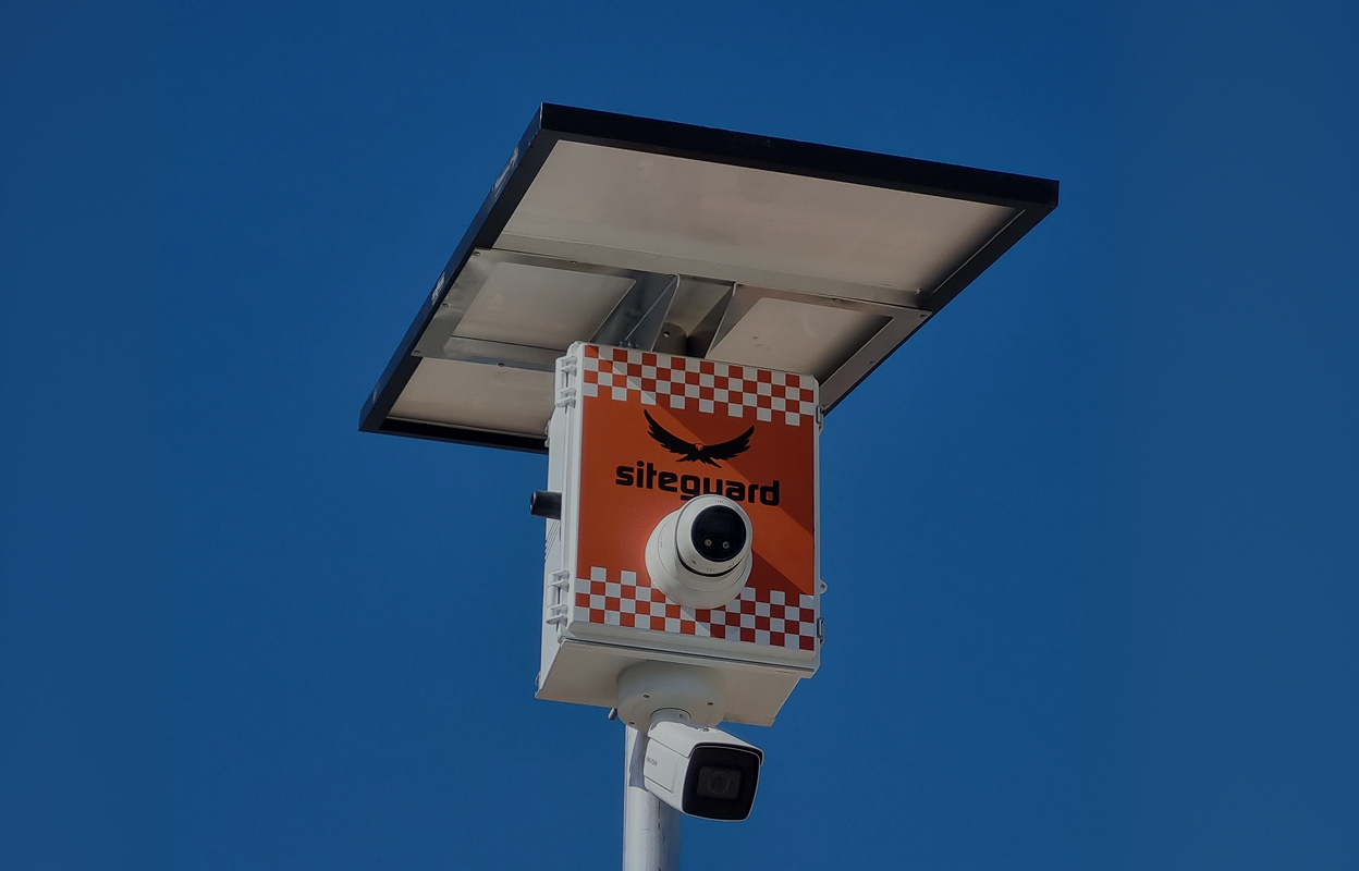 Solar-powered security camera unit with two cameras mounted on a pole against a clear blue sky.
